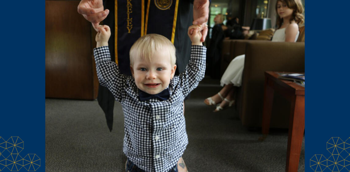 Graduating student at UC Berkeley holding their baby's hands